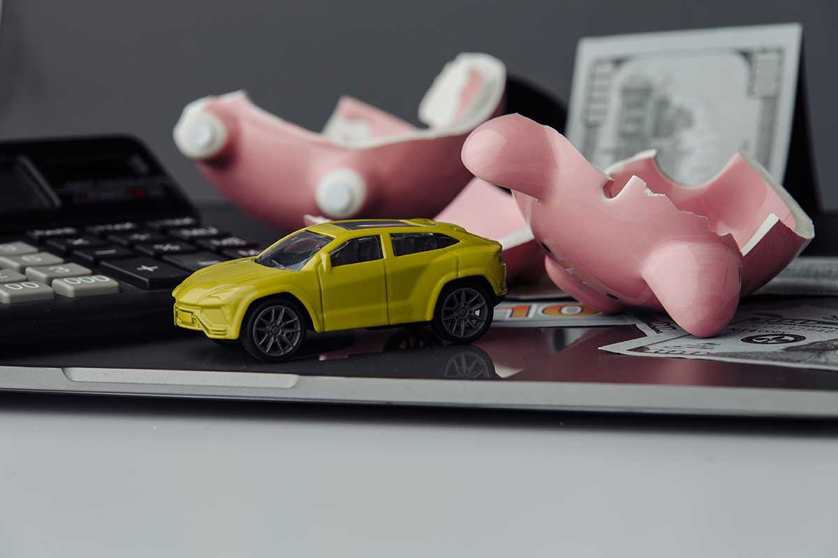 A toy car sitting on top of a calculator with a broken piggy bank in the background.