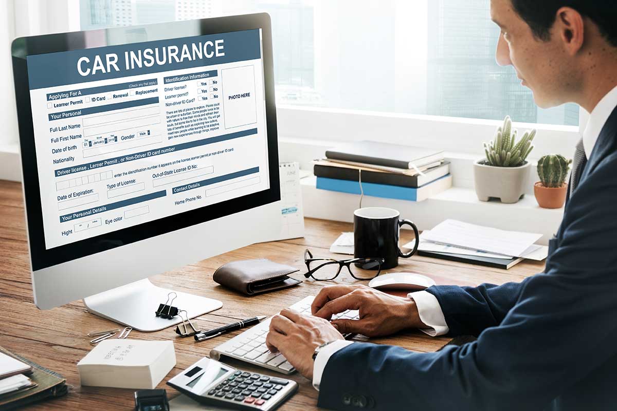 A man sitting at a desk in front of a computer comparing affordable car insurance in Georgia.