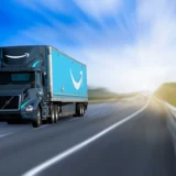 A blue Amazon delivery truck driving at high speed on a highway with a blurred background.