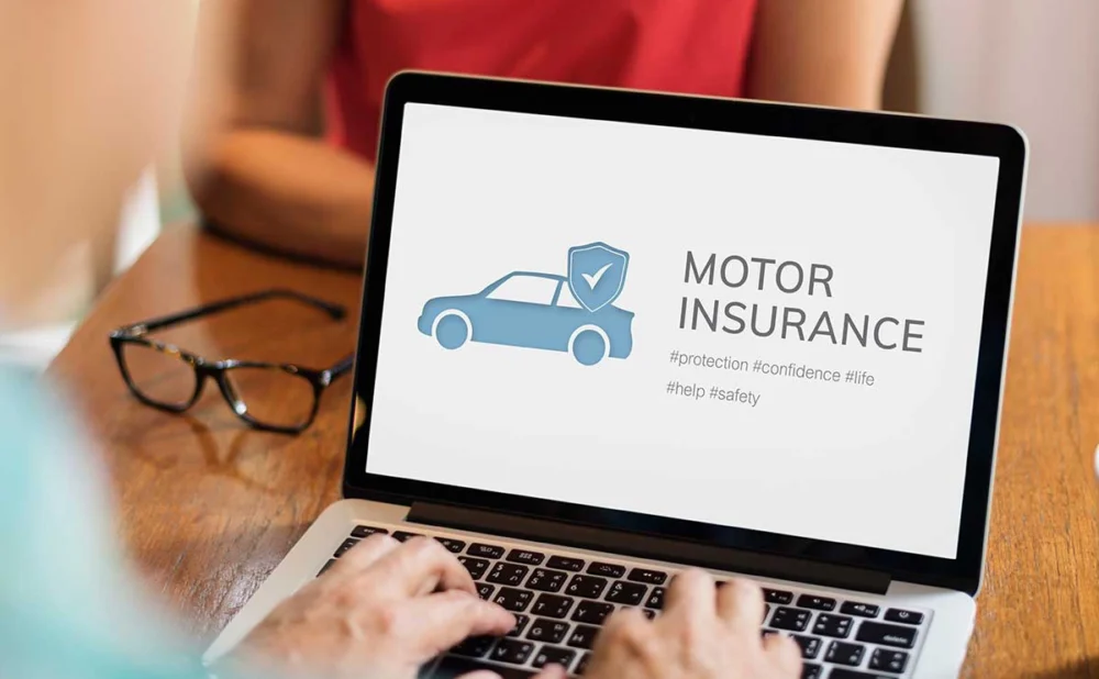 A woman engaged in typing on a laptop, which prominently features the phrase "motor insurance" on its screen.