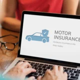 A woman engaged in typing on a laptop, which prominently features the phrase "motor insurance" on its screen.