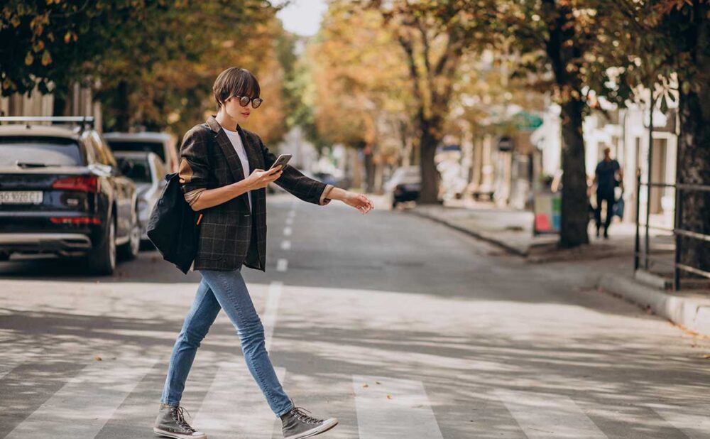 A woman uses her phone while crossing the street, highlighting pedestrian safety concerns in Georgia.