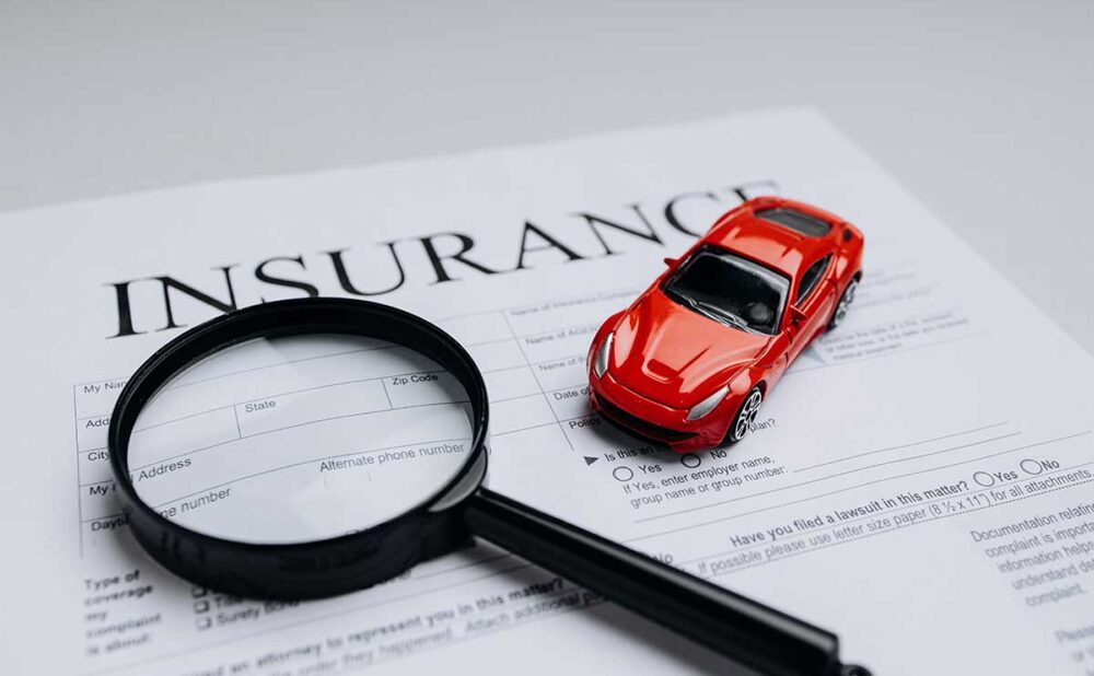 Red toy car and magnifying glass on top of an insurance document, symbolizing the dark side of the 10 worst insurance companies.