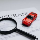 Red toy car and magnifying glass on top of an insurance document, symbolizing the dark side of the 10 worst insurance companies.