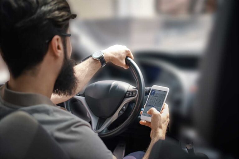 A man drives a vehicle, holding a cell phone, emphasizing the hazards of texting while driving.