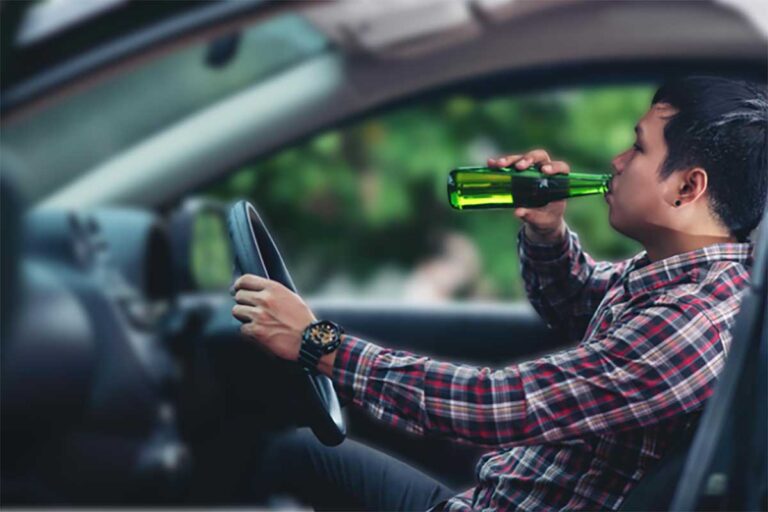 A man driving a car while consuming alcohol from a bottle, illustrating the dangers of drunk driving.