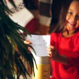 A young girl joyfully holds a note reading "my wishes," symbolizing the power of giving during the holidays.