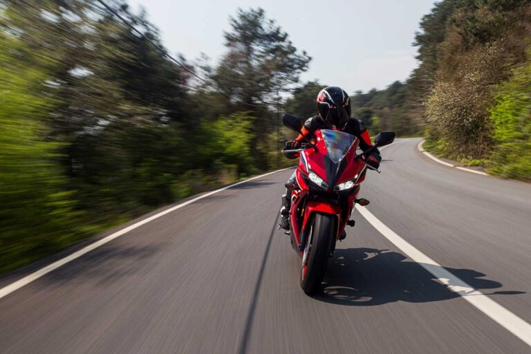 A person rides a red motorcycle on a road, highlighting the importance of safety to prevent common motorcycle injuries in Georgia.