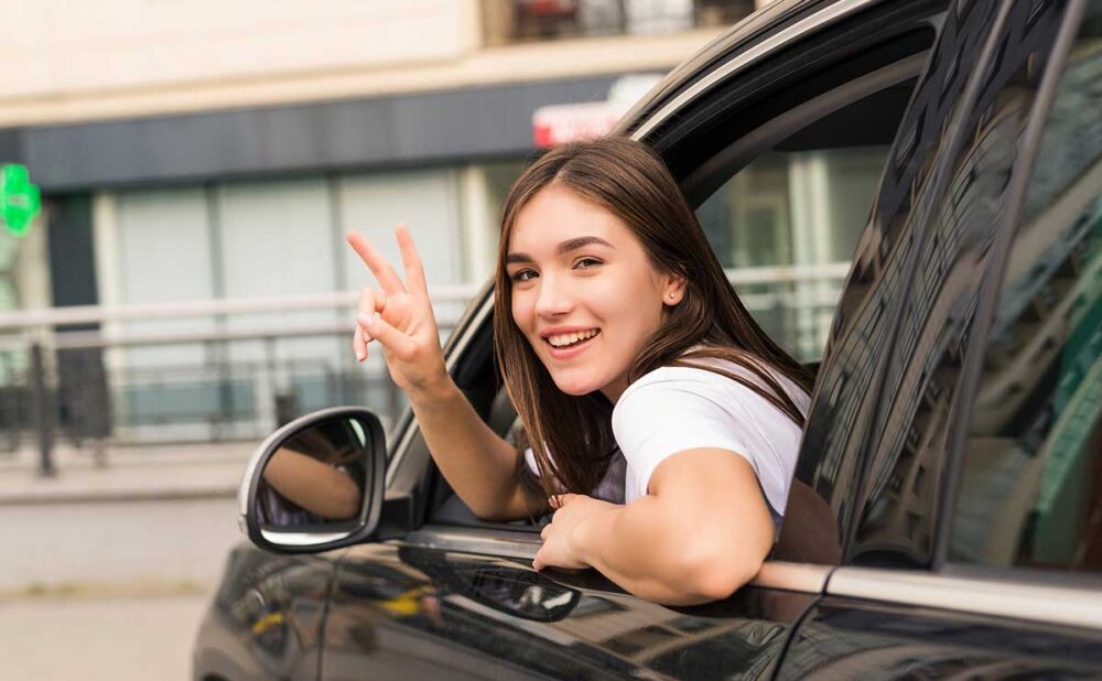 A young woman in the driver's seat of a car, smiling and giving a peace sign, reflecting on the implications of the Georgia Family Purpose Doctrine.