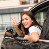 A young woman in the driver's seat of a car, smiling and giving a peace sign, reflecting on the implications of the Georgia Family Purpose Doctrine.