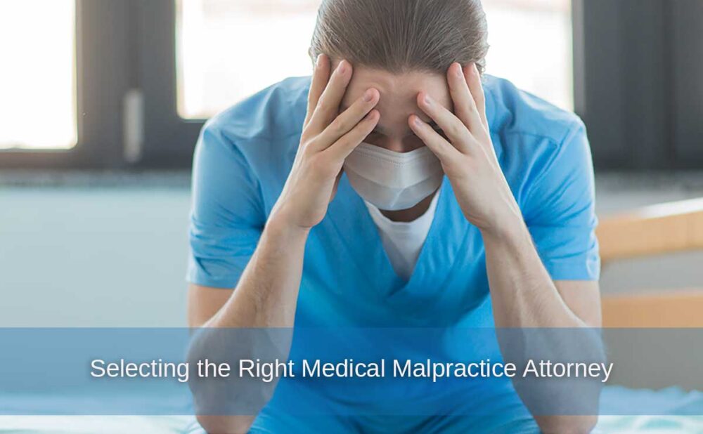 Upset male nurse in scrubs sits on a bed, highlighting the importance of selecting the right medical malpractice attorney for an injury case.