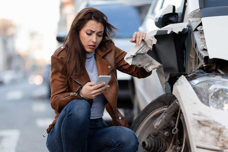 A woman looks at her phone beside a damaged vehicle, considering the implications of the Georgia Family Purpose Doctrine.