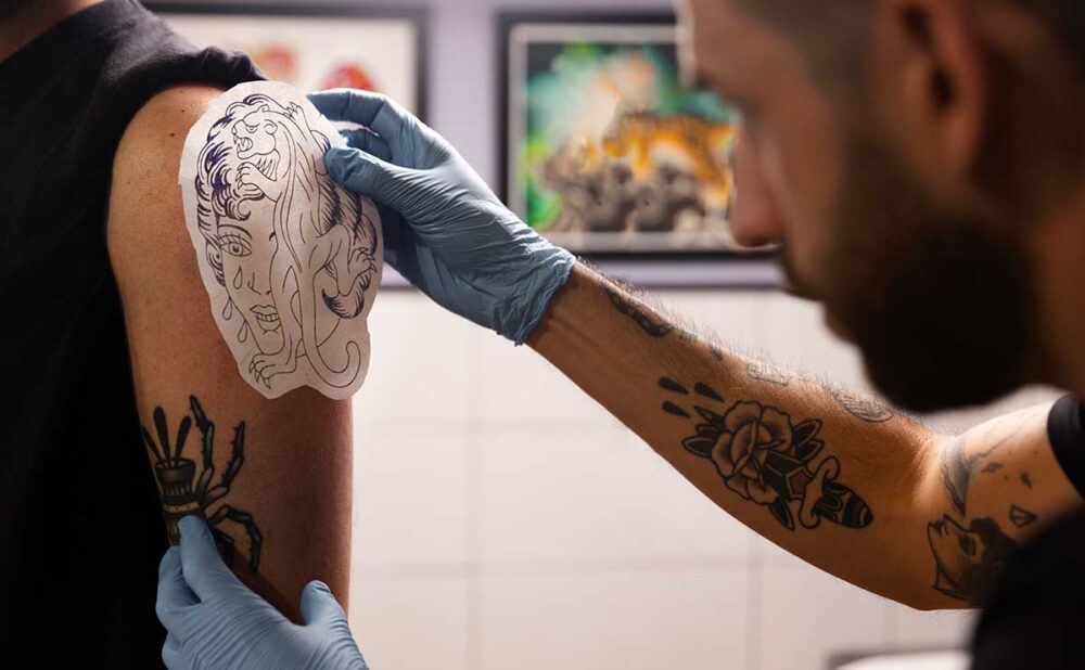 Side view of a man getting a tattoo on his arm, highlighting the importance of understanding tattoo infections before inking.