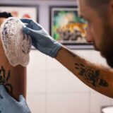 Side view of a man getting a tattoo on his arm, highlighting the importance of understanding tattoo infections before inking.