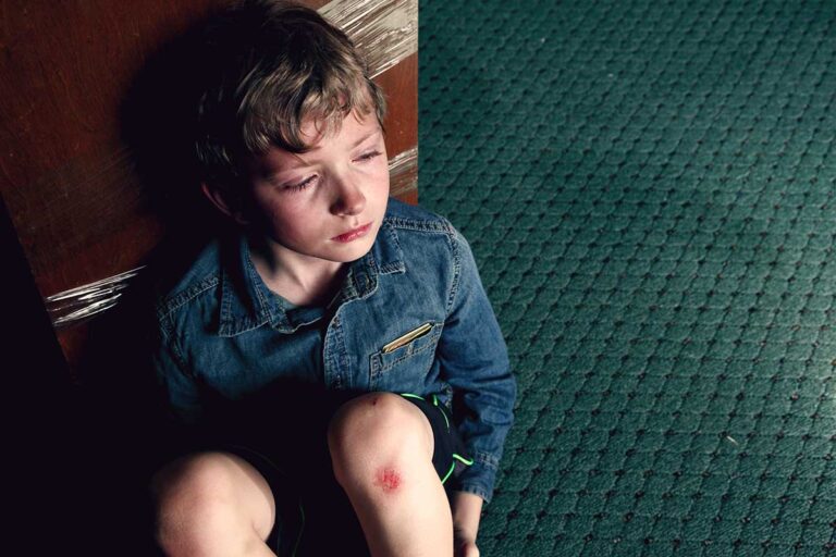 A sad young boy on the floor with an injured knee, conveying a sense of distress in a daycare environment.