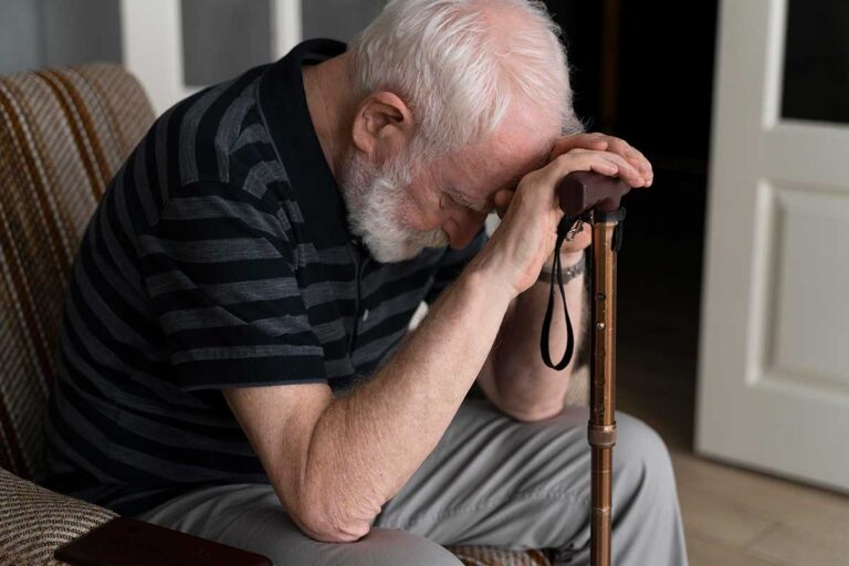 An elderly man sits in a chair, leaning his head on hands on a cane, symbolizing the impact of nursing home abuse in Georgia.